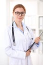 Young brunette female doctor standing with clipboard near window in hospital. Physician ready to examine patient Royalty Free Stock Photo