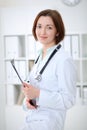 Young brunette female doctor standing with clipboard and smiling in hospital Royalty Free Stock Photo