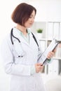 Young brunette female doctor standing with clipboard and smiling at hospital. Royalty Free Stock Photo