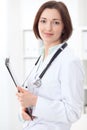 Young brunette female doctor standing with clipboard and smiling at hospital. Royalty Free Stock Photo