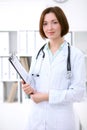 Young brunette female doctor standing with clipboard and smiling at hospital. Royalty Free Stock Photo