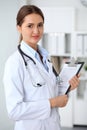 Young brunette female doctor standing with clipboard and smiling at hospital. Physician ready to examine patient Royalty Free Stock Photo