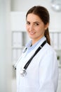 Young brunette female doctor standing with clipboard and smiling at hospital. Physician ready to examine patient Royalty Free Stock Photo