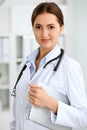 Young brunette female doctor standing with clipboard and smiling at hospital. Physician ready to examine patient Royalty Free Stock Photo