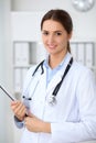 Young brunette female doctor standing with clipboard and smiling at hospital. Physician ready to examine patient Royalty Free Stock Photo