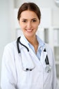 Young brunette female doctor standing with clipboard and smiling at hospital. Physician ready to examine patient Royalty Free Stock Photo