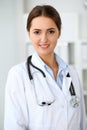 Young brunette female doctor standing with clipboard and smiling at hospital. Physician ready to examine patient Royalty Free Stock Photo