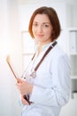 Young brunette female doctor standing with clipboard and smiling in hospital Royalty Free Stock Photo