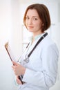 Young brunette female doctor standing with clipboard and smiling in hospital Royalty Free Stock Photo