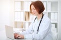 Young brunette female doctor typing on laptop comoputer while sitting at the table in hospital office. Health ca Royalty Free Stock Photo