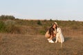 Young brunette girl in beige dress and hat crouched near the samoyed puppy, both looking at left side Royalty Free Stock Photo