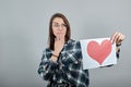 Shocked woman in glasses holds piece of paper with heart in hand, covering mouth Royalty Free Stock Photo