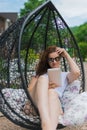 Young brunette girl in denim shorts white top black glasses. Resting in a chair on the outdoor in the hands of a tablet. Royalty Free Stock Photo