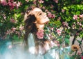 Young girl with looks at a blossoming pink apple tree and smiles Royalty Free Stock Photo