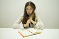 Young brunette girl with flowing hair sits at a table with a diary on the table