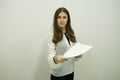 Young brunette girl with flowing hair stands against a white wall holding sheets in one hand Royalty Free Stock Photo