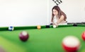 Young brunette girl having a good time playing billiards or aiming for a snooker shot