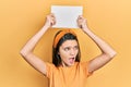 Young brunette girl holding blank empty banner over head angry and mad screaming frustrated and furious, shouting with anger