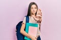 Young brunette girl holding student backpack and books with open hand doing stop sign with serious and confident expression,