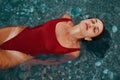 Young brunette girl with long hair in a red bathing suit posing, lying on the sea surface, closing her eyes. Sensuality,femininit Royalty Free Stock Photo