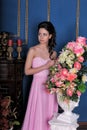 Brunette girl in a pink elegant dress among the flowers in the room