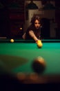 Young brunette girl playing billiard in dark club