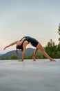 Young brunette girl practicing Camatkarasana or wild pose outdoors.