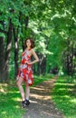 Young brunette girl in red dress posing on alley in summer park against trees Royalty Free Stock Photo