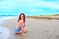 Young brunette girl in striped swimsuit sitting on the beach on the sand Shining bright sun blue sky clouds Royalty Free Stock Photo