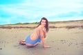 Young brunette girl in striped swimsuit sitting on the beach on the sand Shining bright sun blue sky clouds Royalty Free Stock Photo