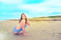 Young brunette girl in striped swimsuit sitting on the beach on the sand Shining bright sun blue sky clouds Royalty Free Stock Photo