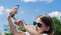 Young brunette girl in summer day enjoying the sun, making selfie portrait. Baby holds a mobile phone in hand and smiles Royalty Free Stock Photo