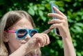 Young brunette girl in summer day walking, enjoying the sun and making selfie portrait. A sweet baby holds a mobile phone in hands Royalty Free Stock Photo