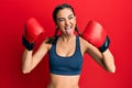 Young brunette girl using boxing gloves wearing braids sticking tongue out happy with funny expression