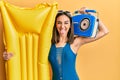 Young brunette girl wearing bikini holding boombox and float sticking tongue out happy with funny expression