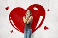 Young brunette girl wearing casual jeans and t-shirt smiling and touching face with big red heart drawn on white wall