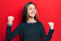 Young brunette girl wearing casual sweater very happy and excited doing winner gesture with arms raised, smiling and screaming for