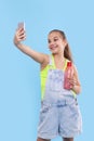 A young brunette girl wearing  denim overalls shorts stands with a phone and with a bottle of water Royalty Free Stock Photo