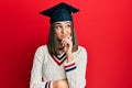 Young brunette girl wearing graduation cap serious face thinking about question with hand on chin, thoughtful about confusing idea Royalty Free Stock Photo