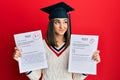 Young brunette girl wearing graduation cap showing exams smiling looking to the side and staring away thinking Royalty Free Stock Photo