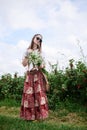 Young brunette hippie woman, wearing boho style clothes and sunglasses, standing on green currant field, holding camomiles` Royalty Free Stock Photo
