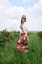 Young brunette hippie woman, wearing boho style clothes and sunglasses, standing on green currant field, posing for picture. Royalty Free Stock Photo