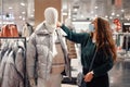 Young brunette lady in face mask chooses warm clothes during pandemic, buying puffy winter jacket Royalty Free Stock Photo