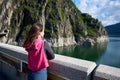 Young brunette looking far into the distance admiring the beauty of green grassy rocks and Vidraru lake in Romania