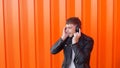 Young caucasian man in music headphones listens to music and dances on orange background, prance, slow motion, earpieces