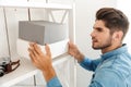 Young brunette man holding boxes while standing by shelving in office