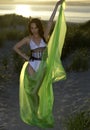 Young brunette model posing in design bikini and holding green floating beach cover up on sunset time Royalty Free Stock Photo