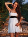 Young brunette model at the white dress staying on the stairs with green trees  with closed eyes Royalty Free Stock Photo