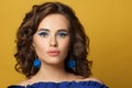 Young brunette model woman with curly bob haistyle and blue earrings on vivid yellow background Royalty Free Stock Photo