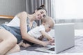 Young brunette mom with a small child in front of a laptop in bed. The baby prevents mom from working from home. Self-isolation Royalty Free Stock Photo